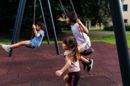 three girls playing at children playground with swings in public parkの写真素材