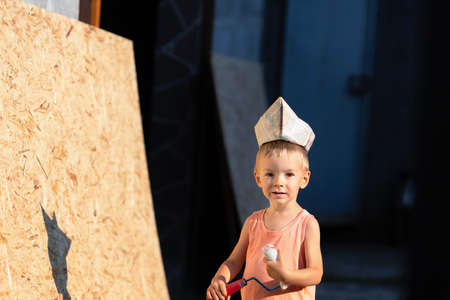 Little blond boy plays builder.Child paints the wall.Summer holidays in the village.Boy and osb panel.の写真素材