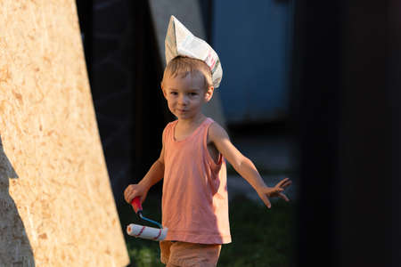 Little blond boy plays builder.Kid in T-shirt, shorts and garrison cap holds a construction...