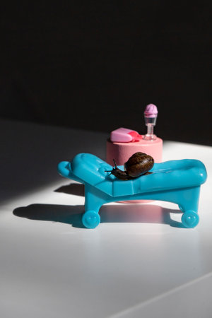 A snail in the sun on a chaise longue.A blue chaise longue and a pink cocktail table.Summer holidays on the beach.の写真素材