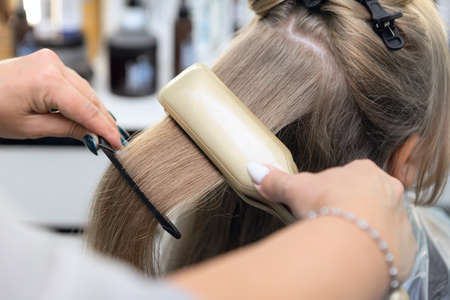 Styling girls hair with a hot straightening iron.Hair straightenerの写真素材