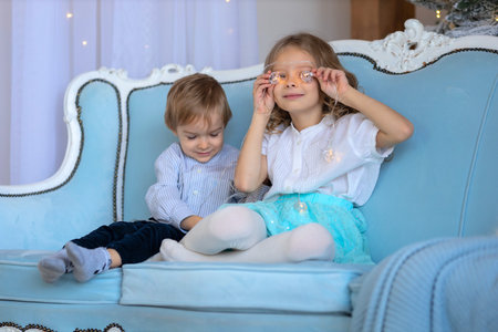 A boy and a girl play on a blue sofa against the background of garlandsの写真素材