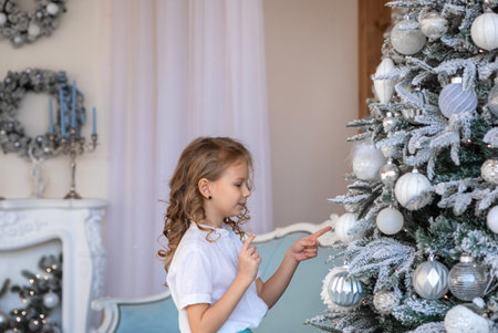 A blonde girl reaches for the Christmas tree to hang a toyの写真素材