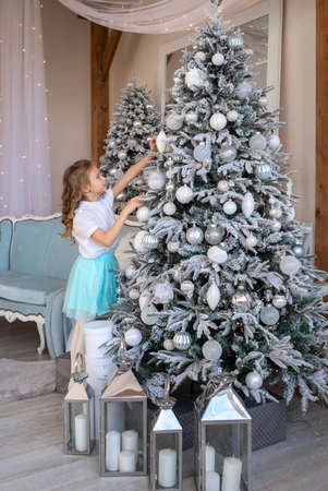 A blonde girl reaches for the Christmas tree to hang a toyの写真素材