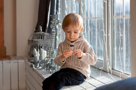 A blond-haired boy is sitting near the windowの写真素材