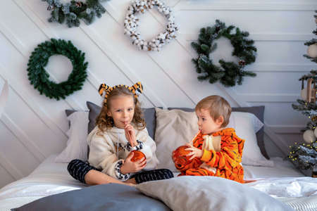 Children in kigurumi pajamas sit on the bed and hold toy glass ballsの写真素材