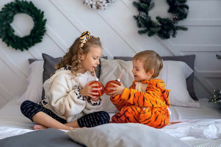 Children in kigurumi pajamas sit on the bed and hold toy glass ballsの写真素材