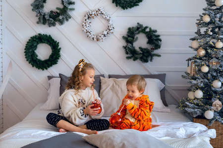 Children in kigurumi pajamas sit on the bed and hold toy glass ballsの写真素材