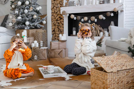 Children in kigurumi pajamas sit on the floor and drink cocoa and cookiesの写真素材