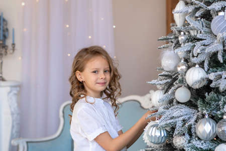 A blonde girl with curly hair decorates a Christmas treeの写真素材