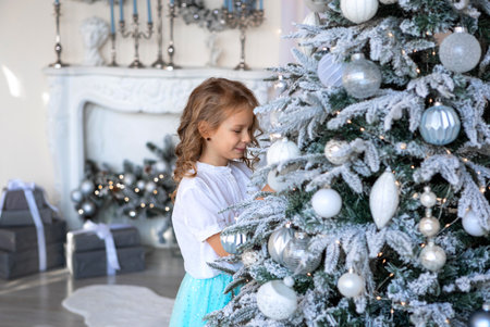 A blonde girl reaches for the Christmas tree to hang a toyの写真素材