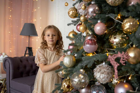 A blonde girl reaches for the Christmas tree to hang a toyの写真素材