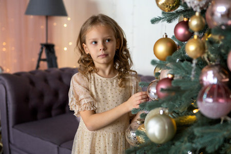 A blonde girl reaches for the Christmas tree to hang a toyの写真素材