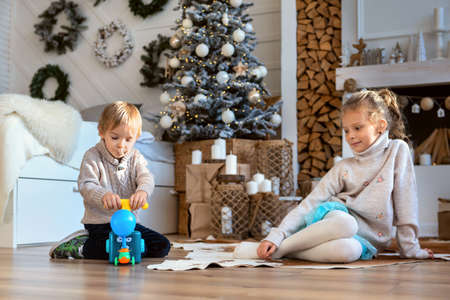 A boy and a girl are passionate about gifts on the background of a decorative fireplaceの写真素材