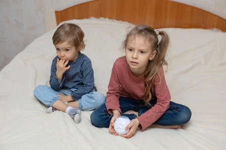 A boy and a girl are sitting on a bed with a cube-shaped projectorの写真素材