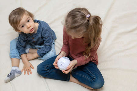 A boy and a girl are sitting on a bed with a cube-shaped projectorの写真素材