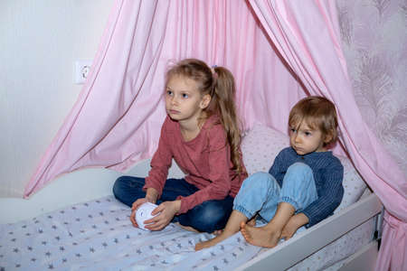 A boy and a girl are sitting on a bed with a cube-shaped projectorの写真素材