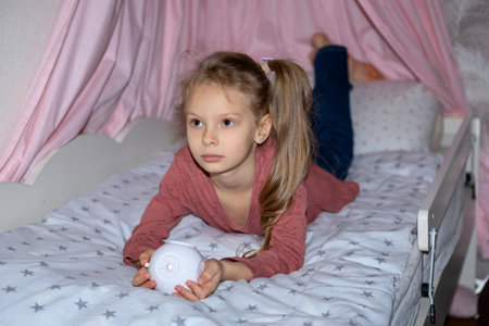 The girl has a small portable projector in her hands for watching moviesの写真素材