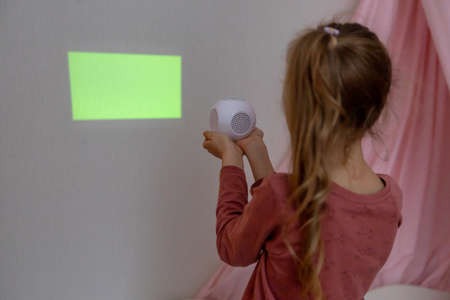 A girl in the childrens room looks through a projector at a green screenの写真素材