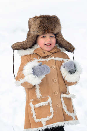 A kid in a winter fur coat, hat and felt boots in a snow-covered forestの写真素材