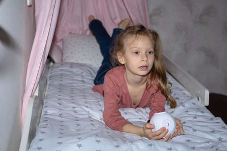 The girl has a small portable projector in her hands for watching moviesの写真素材