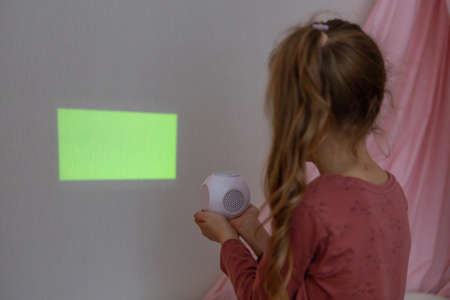 A girl in the childrens room looks through a projector at a green screenの写真素材