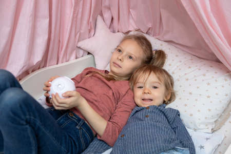A boy and a girl are lying on the bed with a projectorの写真素材
