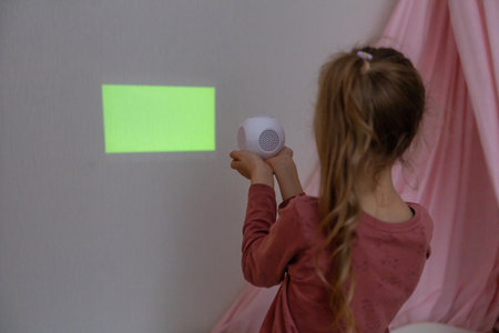 A girl in the childrens room looks through a projector at a green screenの写真素材