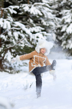 A girl in a funny fur hat and sheepskin coat is playing in a snowy forestの写真素材