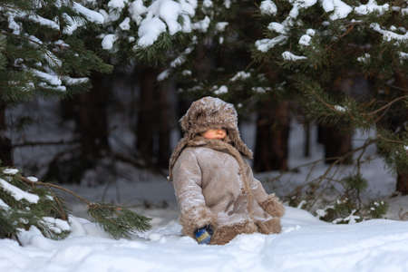 A cute boy in a fur coat and a hat with earflaps walks in winterの写真素材