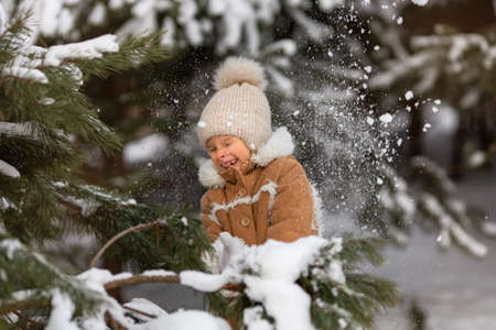 A girl in a winter hat and sheepskin coat is playing in a snowy forestの写真素材