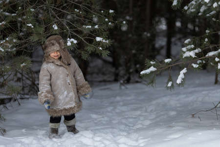 A cute boy in a fur coat and a hat with earflaps walks in winterの写真素材