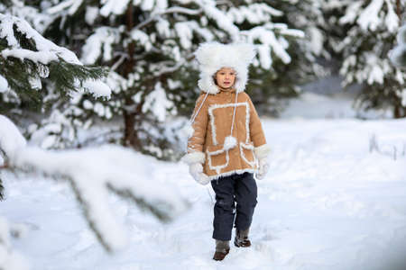 A girl in a fur hat and fur coat is playing in a snowy forestの写真素材