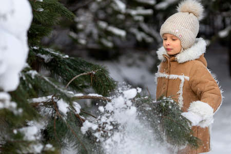 A girl in a winter hat and sheepskin coat is playing in a snowy forestの写真素材