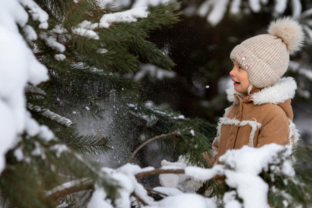A girl in a winter hat and sheepskin coat is playing in a snowy forestの写真素材