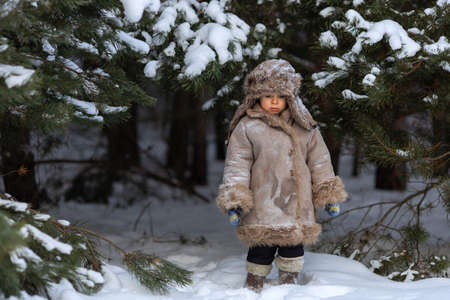 A cute boy in a fur coat and a hat with earflaps walks in winterの写真素材
