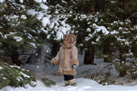 A cute boy in a fur coat and a hat with earflaps walks in winterの写真素材