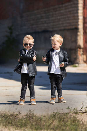 Twin brothers in leather jackets and sunglasses.Two identical blond boysの写真素材