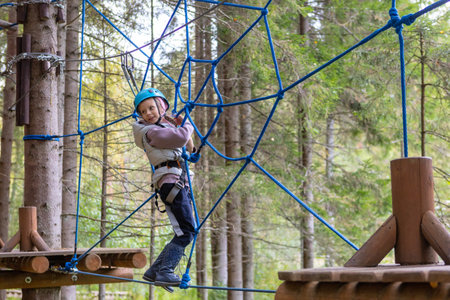 A child wearing a helmet and safety ropes will pass rope trails in a sports parkの写真素材