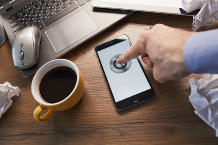 business concept with man pressing his phone, coffee on the side and laptop on wooden table