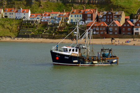 A commercial fishing boat heading out to sea from the harbor in Whitby, United Kingdom