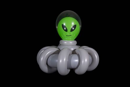 Inflated balloon sculpture of an alien inside the clear cockpit of a gray spaceship flying through outer space.の写真素材