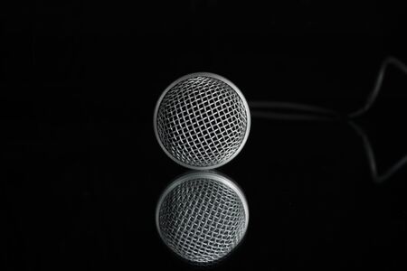 Silver microphone head against a black background with it's reflection in a mirror below it showing the tiny diamonds in the grid of the wire mesh.の写真素材