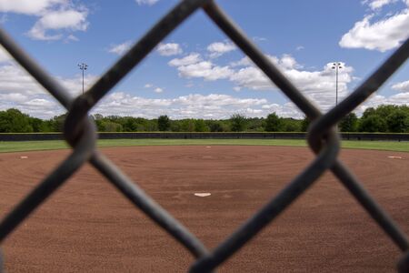 Looking out across a baseball field from behind home plate through one of the diamond shaped openings in a chain link fence on a sunny spring afternoon.の写真素材