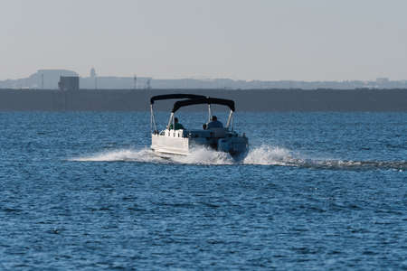 Pontoon boat with twin canopies heading out for a day on the lake in the warm glow of the early...