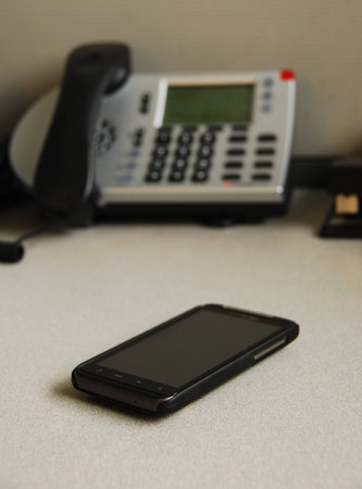 A cell phone in front of a regular phone on a deskの写真素材
