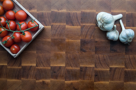 Cherry tomatoes and garlic on wooden brown handmade cutting boardの写真素材