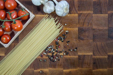 cherry tomatoes, pasta spaghetti and garlic on a wooden brown handmade cutting boardの写真素材