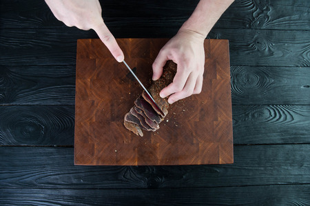 Portion of Beef Jerky cutting into slice on a cutting table with a kitchen knife on a vintage wooden backgroundの写真素材