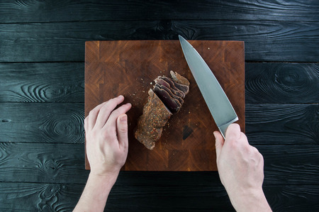 Portion of Beef Jerky cutting into slice on a cutting table with a kitchen knife on a vintage wooden backgroundの写真素材